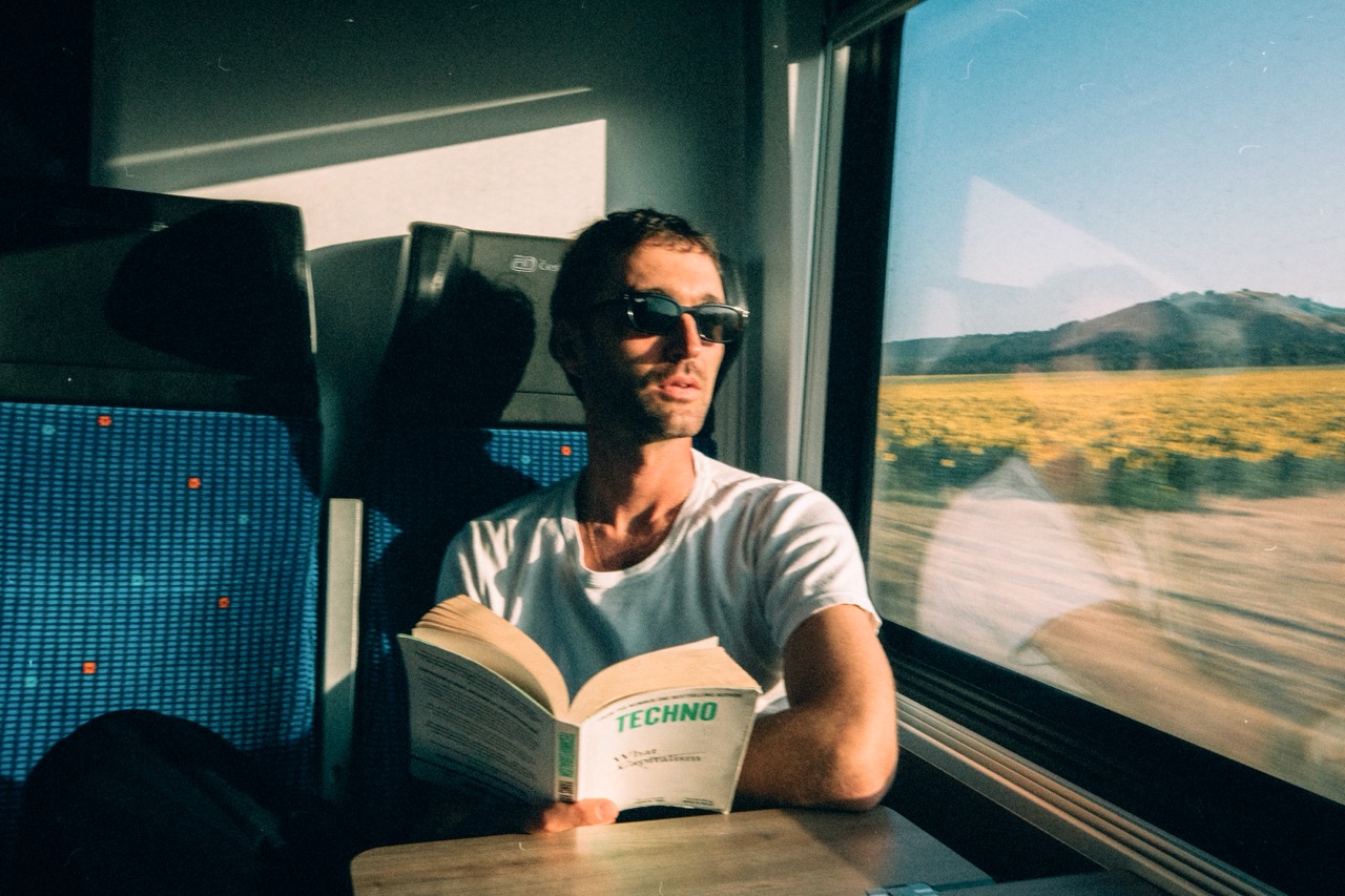 坐在歐洲火車窗邊看書的旅人，窗外是向日葵花田，Interrail 品牌形象照 The Interrail Effect